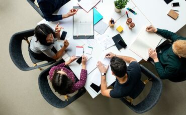 Top-View-Aufnahme von Geschäftskollegen, die über ein neues Projekt im Büro diskutieren. Gruppe junger Männer und Frauen, die am Tisch brainstormen, während sie an einem neuen Projekt arbeiten.  Vielen Dank Dieses Foto wurde erfolgreich heruntergeladen. (