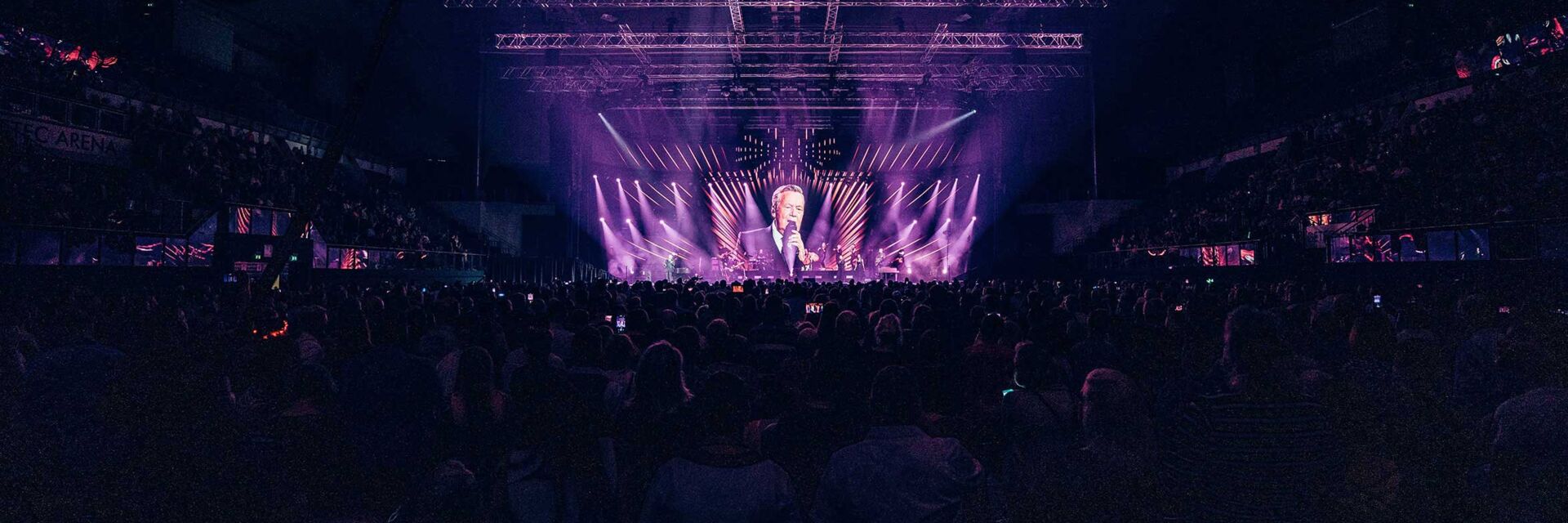 Roland Kaiser gibt ein Konzert in der GETEC-Arena. Das Publikum ist von hinten zu sehen und das Bild erscheint in violetten Farben